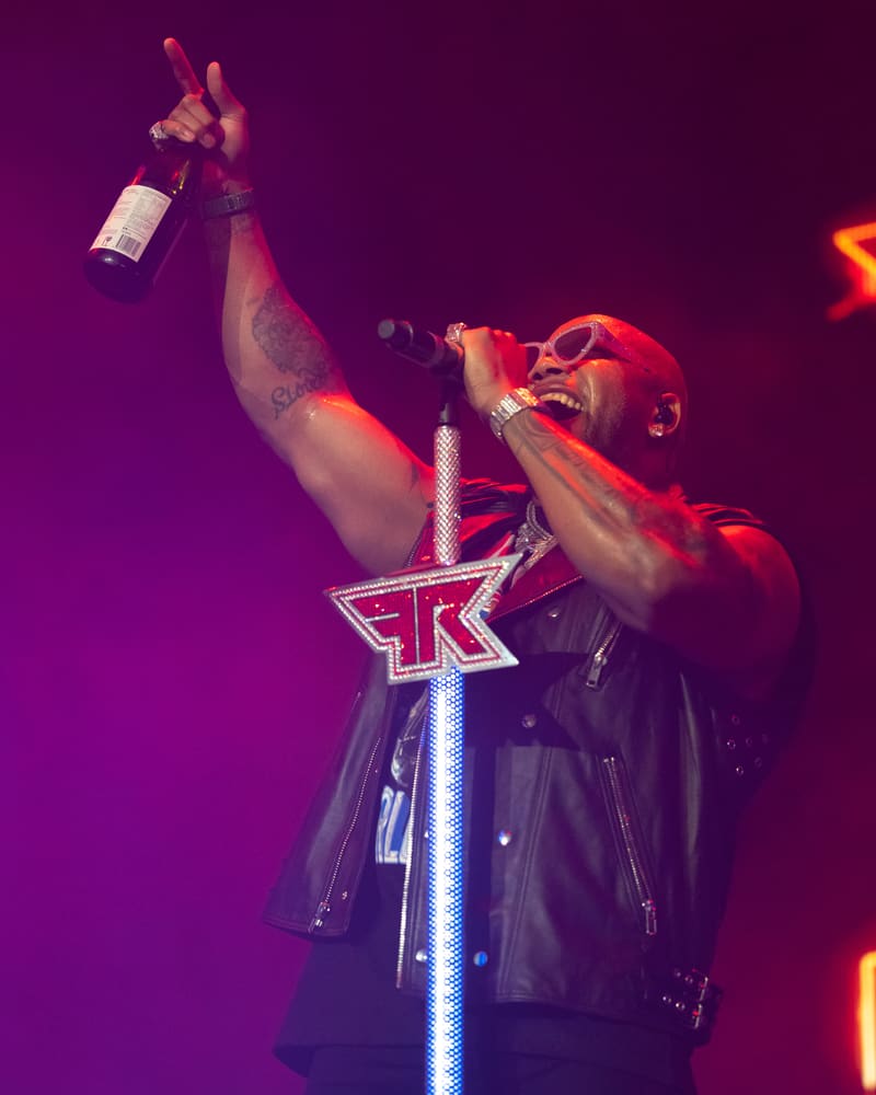 Performer on stage holding a bottle aloft beneath purple and red stage lighting during Fridayz Live.