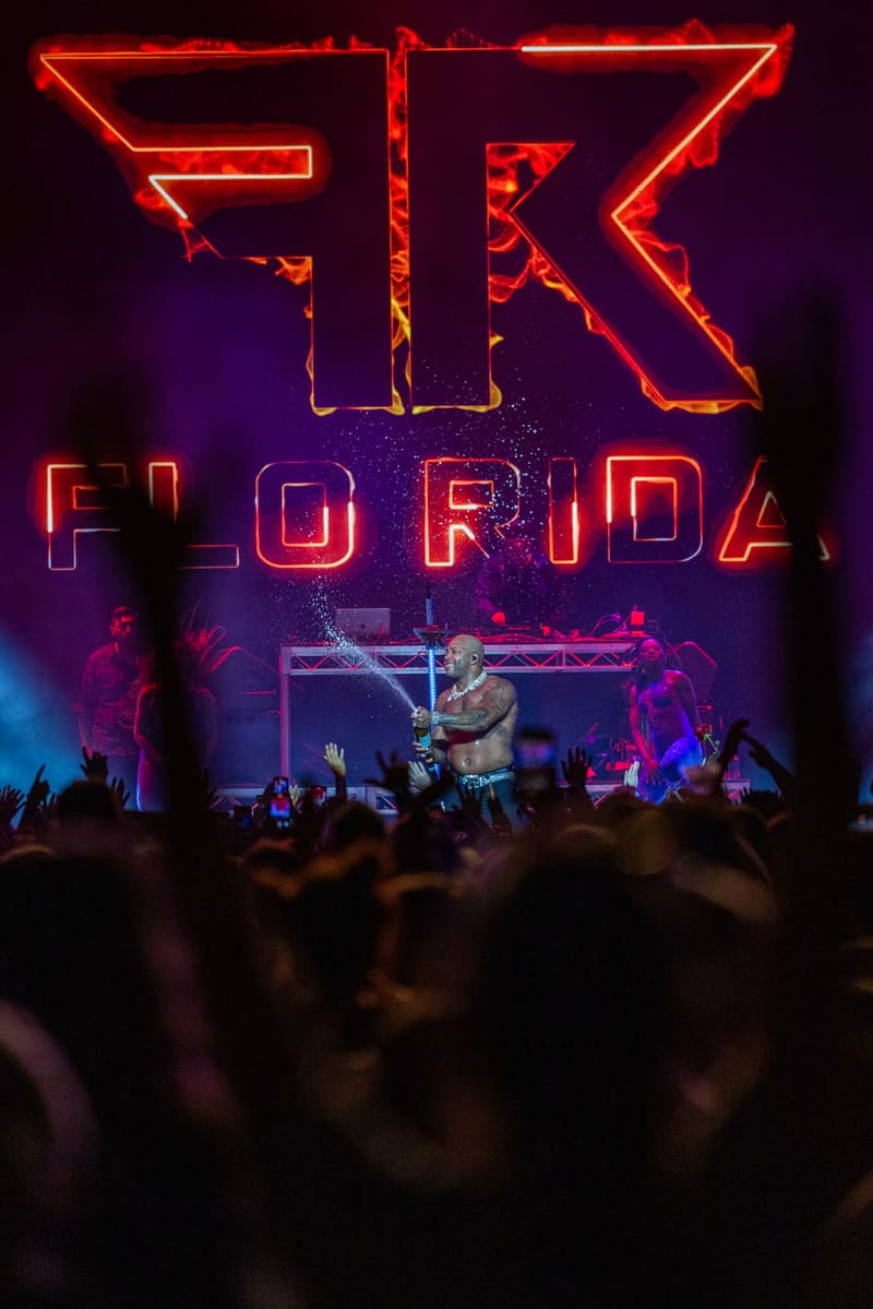 Performer on stage beneath glowing neon "Flo Rida" signage, silhouetted crowd in foreground.