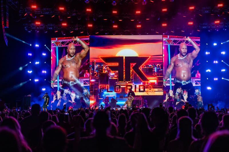Silhouetted crowd watching large LED screens displaying a performer during a nightclub event with blue and red stage lighting.