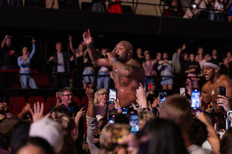 Performer on stage surrounded by audience members with raised hands and phones during Fridayz Live concert.