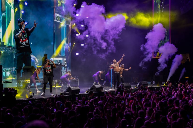 Stage filled with purple and yellow smoke during a live concert performance with crowd visible in foreground.