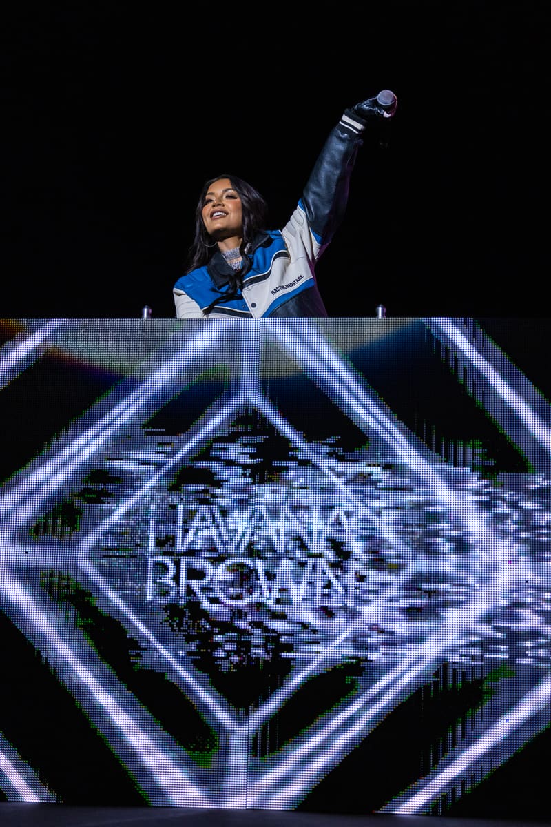 DJ in blue and white jacket raising fist at booth lit by neon geometric display during Havana Brown – Fridayz Live performance.