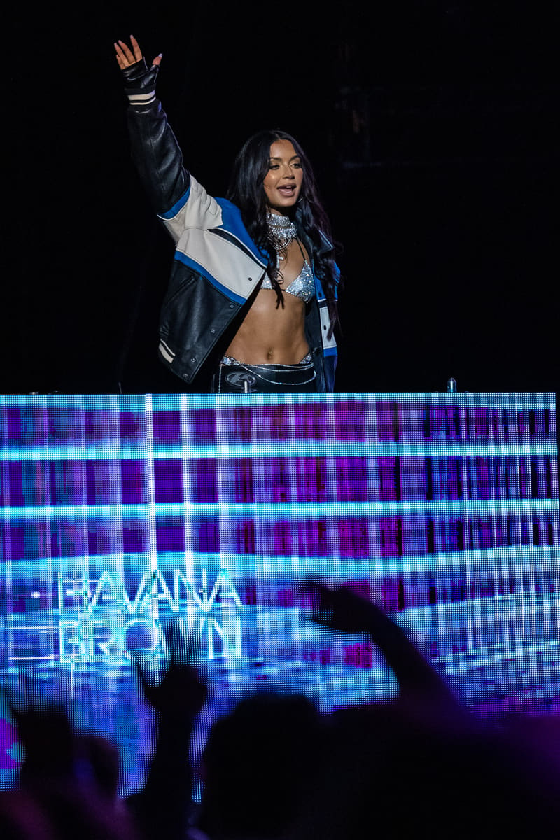 Performer on stage with raised fist wearing a black and blue jacket, illuminated by neon blue and purple LED lighting.