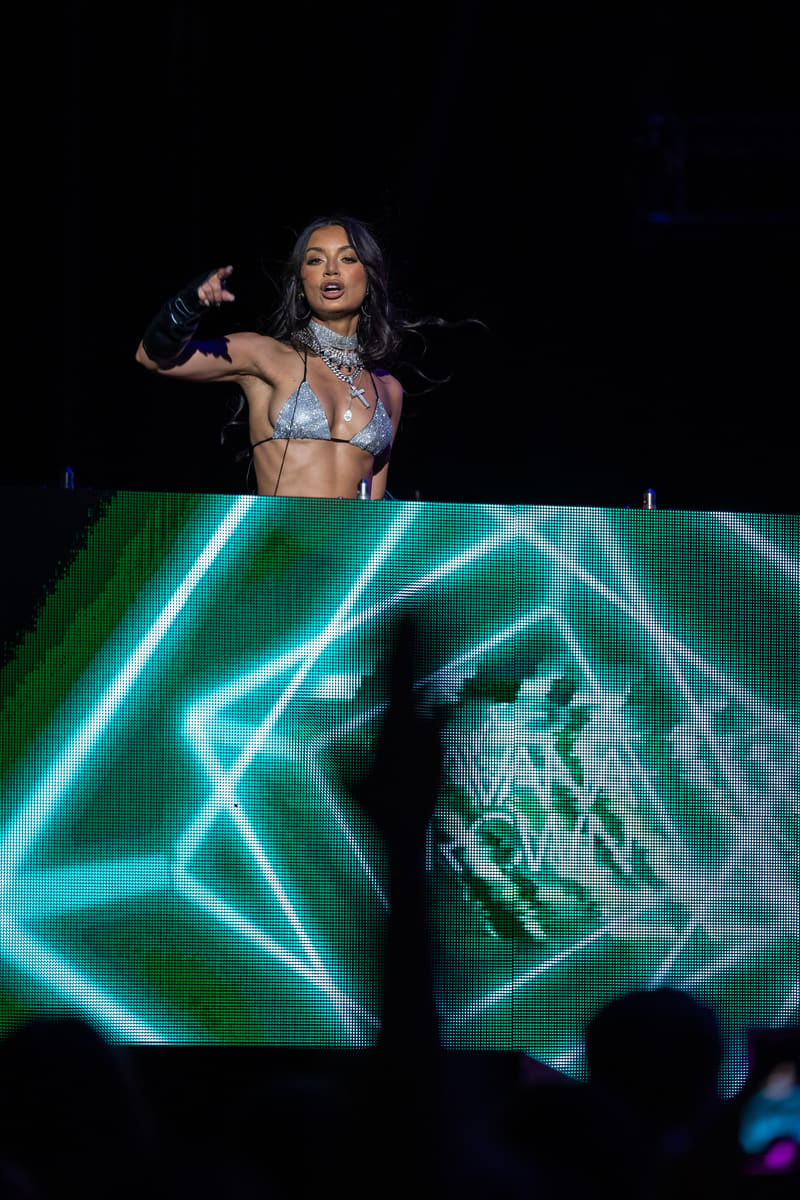 Performer in sequined bikini top gestures expressively above neon geometric stage visuals during Fridayz Live.