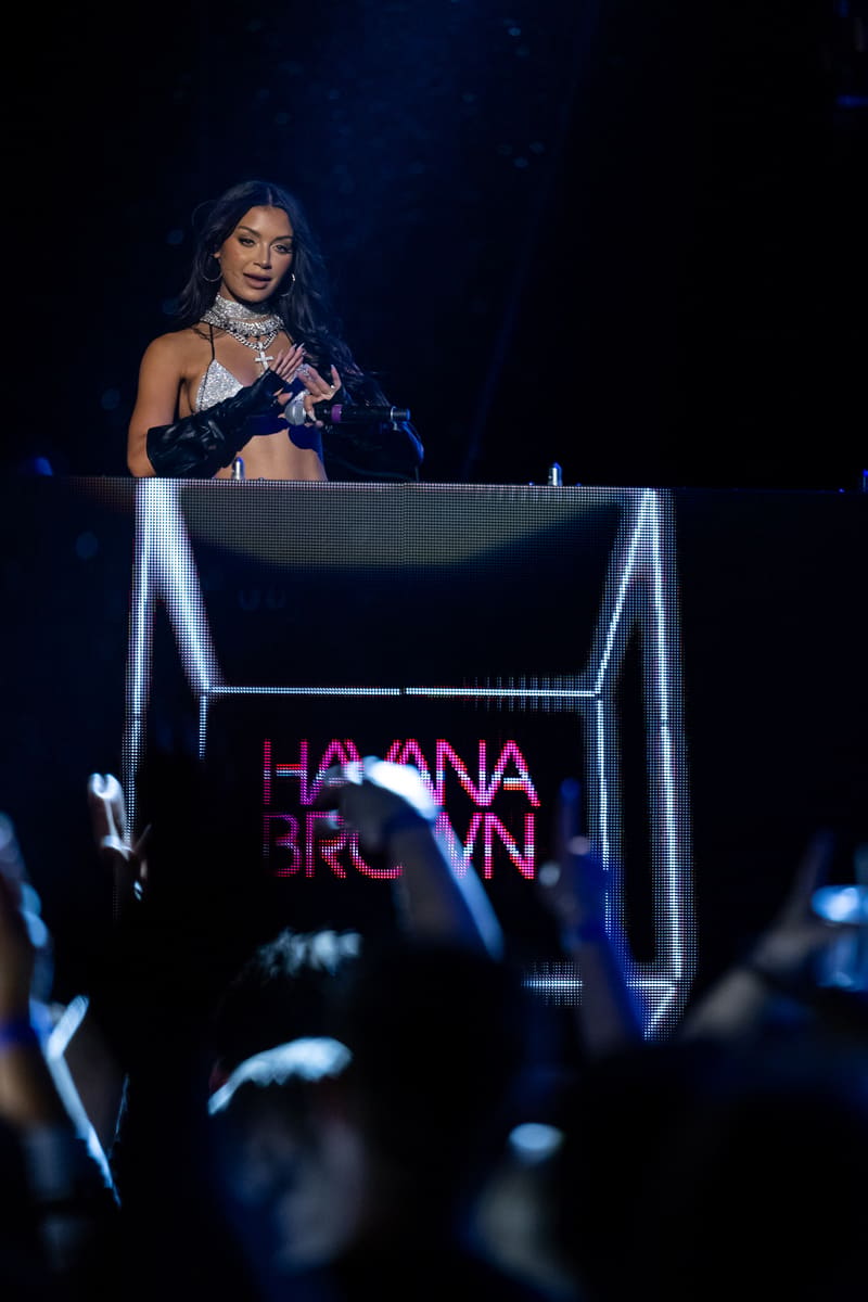 Performer at an illuminated DJ booth with "Havana Brown" signage during a live stage performance.