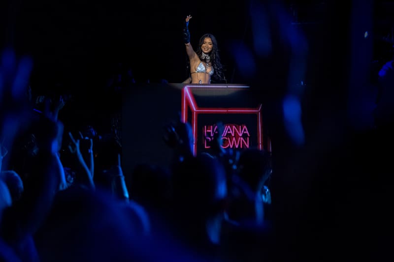 DJ at illuminated booth performing to crowd under blue stage lighting.