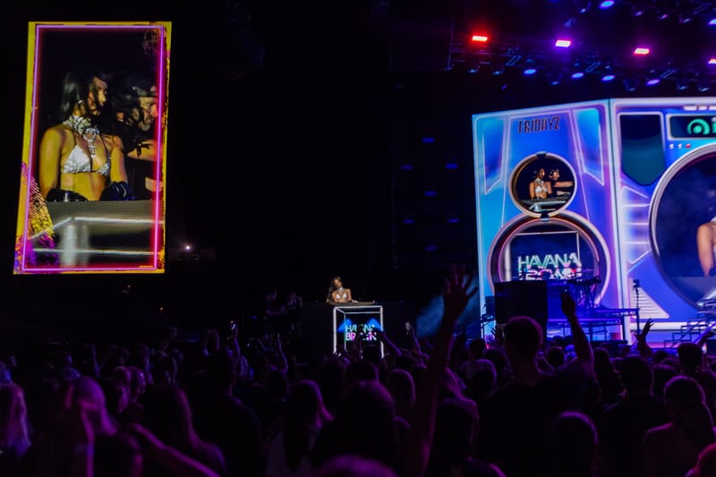 Crowd with raised hands and phones facing a stage with neon-framed screens during a nightclub performance.