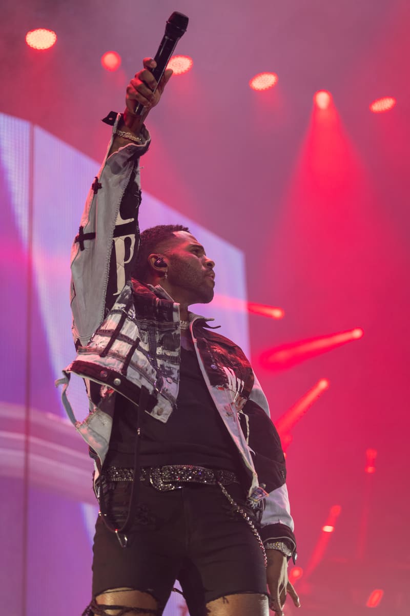 Performer on stage holding a microphone aloft, bathed in pink and magenta stage lighting.