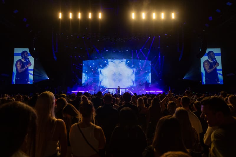Crowd of concertgoers faces a stage with large screens and blue lighting during a Jason Derulo performance.