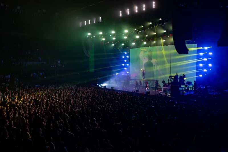 Large crowd facing an illuminated stage with green and blue lighting during a concert performance.