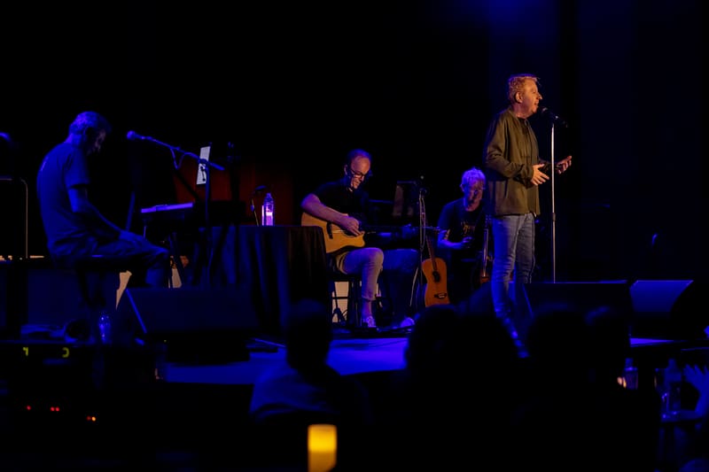 Irish vocalist performs with acoustic band under blue stage lighting before an audience.
