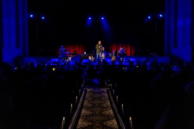 Tommy Fleming performs on stage beneath blue spotlights with a full band, viewed from the audience.