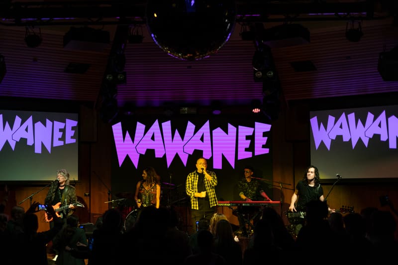 Band performing on stage beneath purple "Wa Wa Nee" signage, bathed in purple stage lighting.
