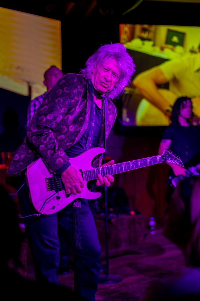 Guitarist performing on stage bathed in magenta stage lighting during a live band performance.