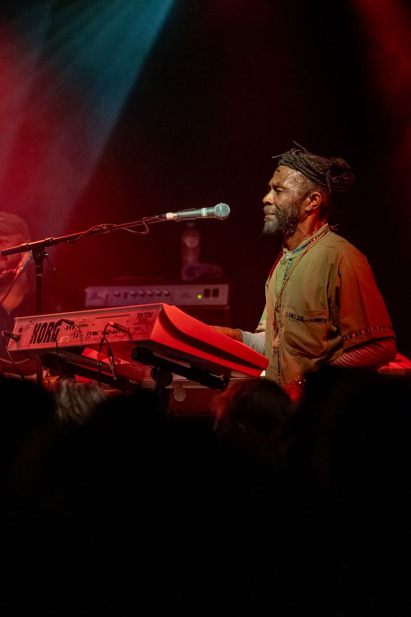 Musician performs at keyboard under red and blue stage lighting during The Original Wailers concert.