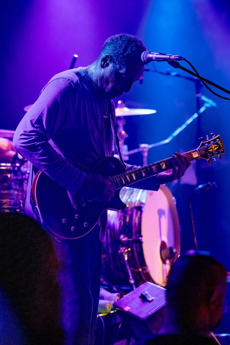 Guitarist and vocalist performs at microphone under purple and blue stage lights during The Original Wailers concert.