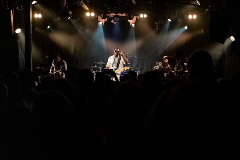 The Original Wailers perform on stage beneath dramatic spotlights, silhouetted audience in foreground.
