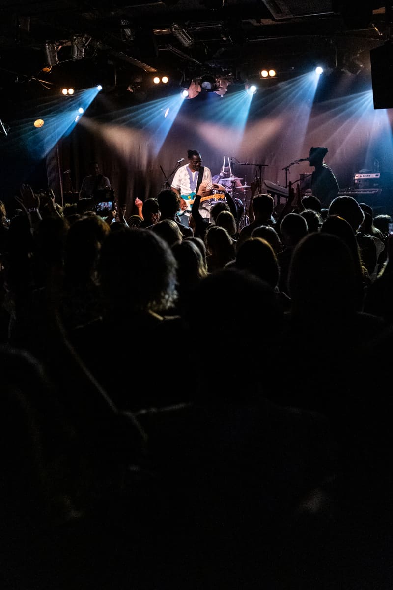 Band performs on stage bathed in blue spotlights whilst crowd watches from the venue floor.