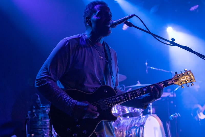 Guitarist performs at microphone under blue stage lighting during live concert.