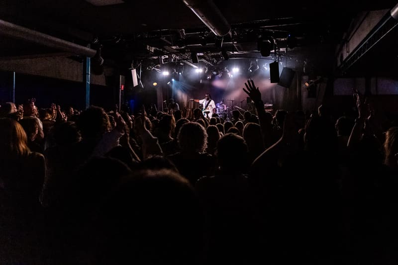 Crowd of audience members with hands raised watching a reggae band perform on stage under bright spotlights.