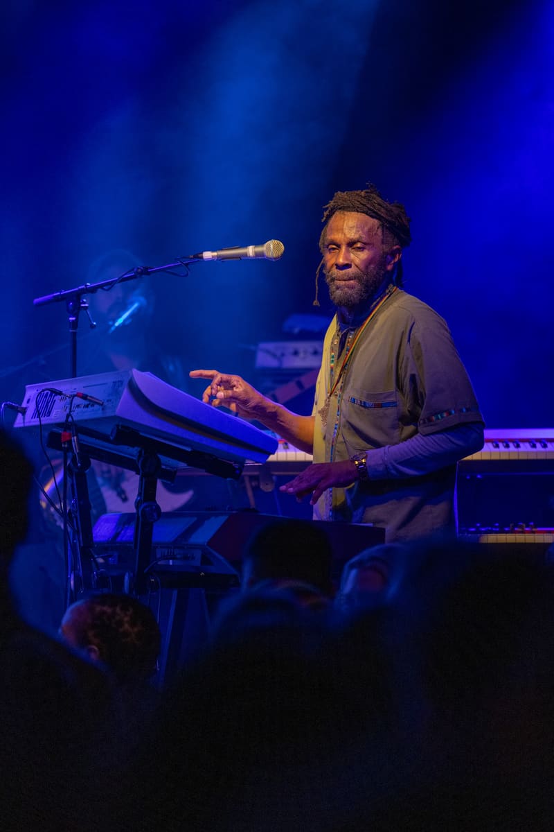 Musician performs at keyboard under blue stage lighting during The Original Wailers concert.