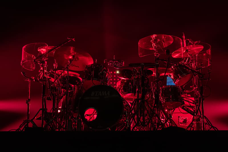 Drummer silhouetted behind a drum kit illuminated in deep red stage lighting.