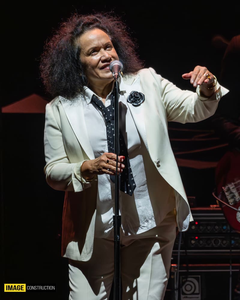 Performer in cream suit and dark shirt singing at microphone on stage during Forever Enz 2026 tour.