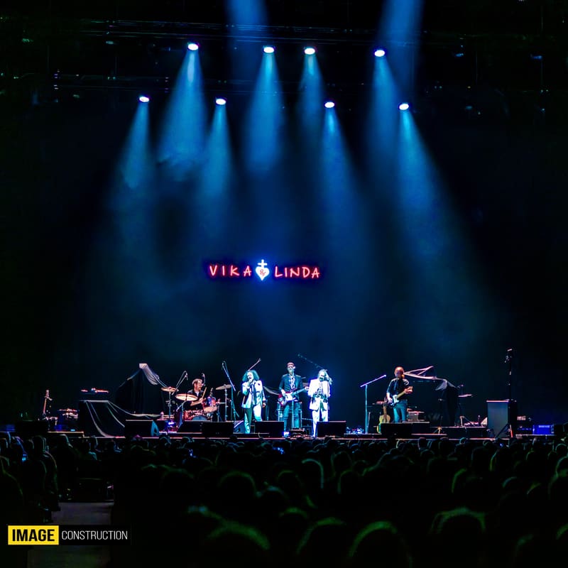 Band members perform on stage beneath blue spotlights with "Vika & Linda" logo displayed above.