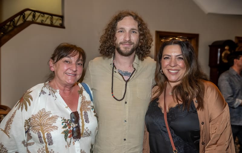 Three people pose together at a gallery opening, smiling at the camera in an indoor venue.