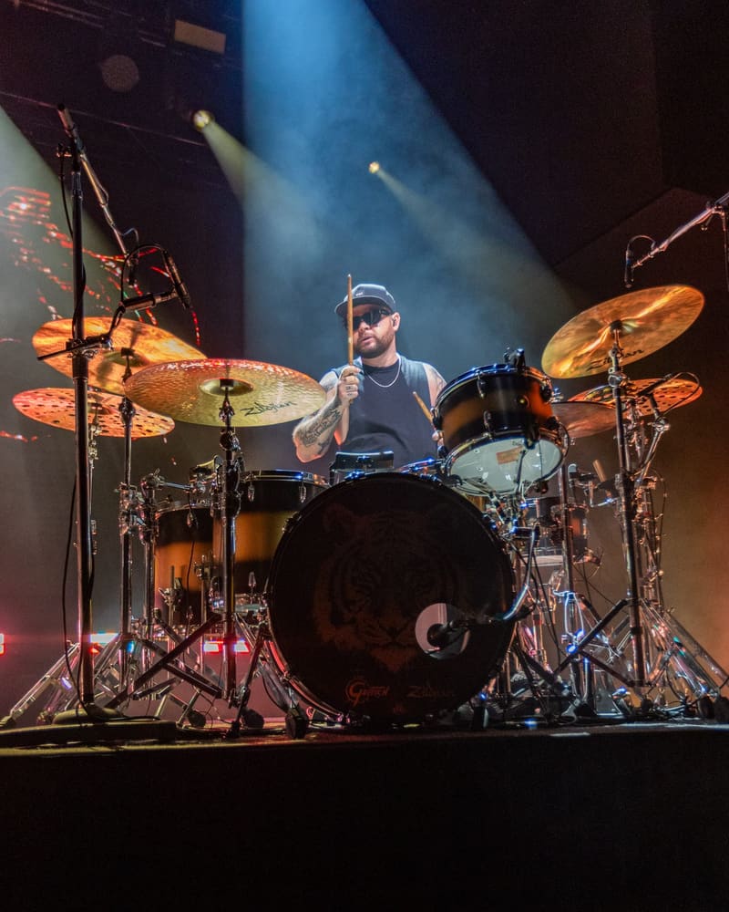 Drummer performing on stage with blue spotlights and cymbals illuminated during a rock concert.