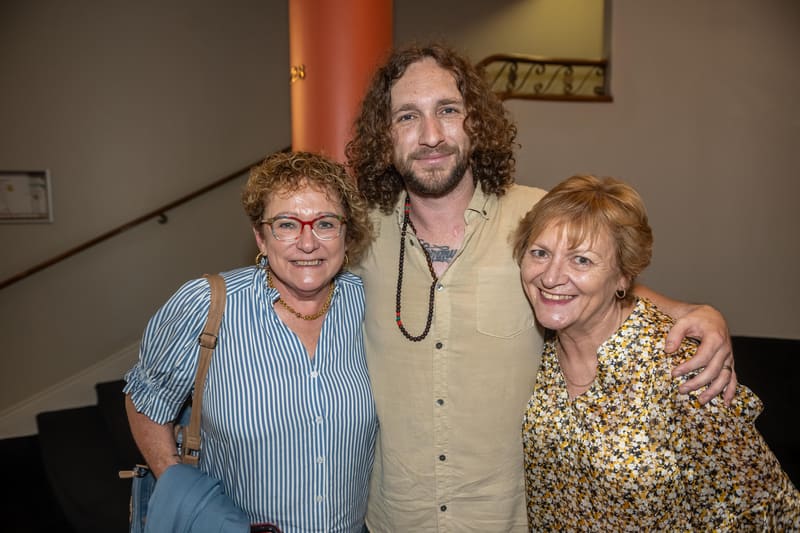 Three people pose together in a gallery space, smiling at the camera.