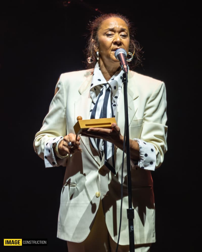 Singer in cream suit and patterned tie performing at microphone during the Forever Enz 2026 tour.
