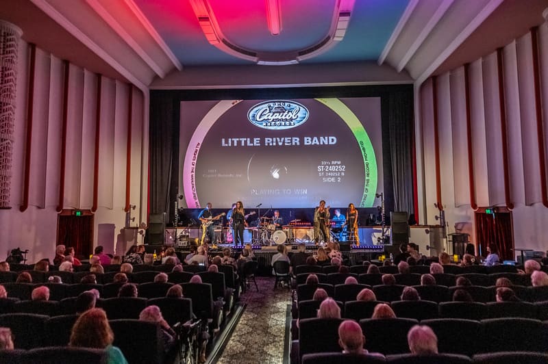 Little River Band performs on stage beneath neon-lit arch to seated audience in theatre venue.