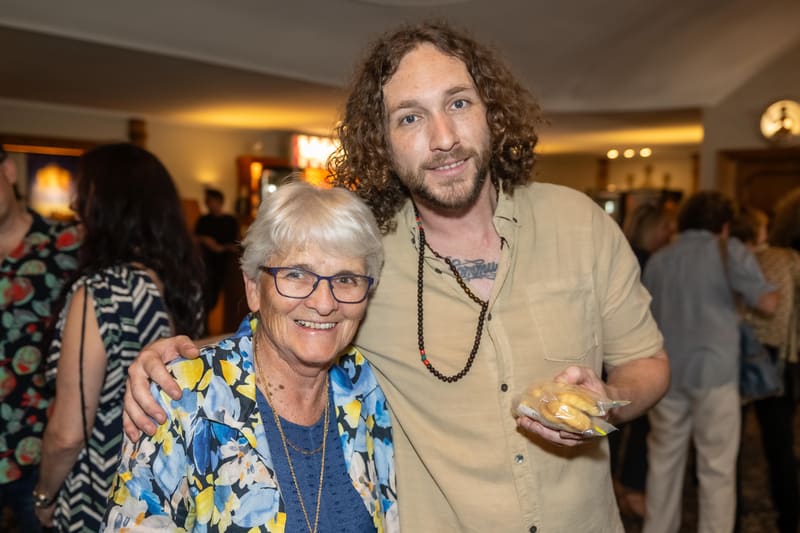 Man with curly hair and woman wearing glasses pose together at a gallery opening reception.