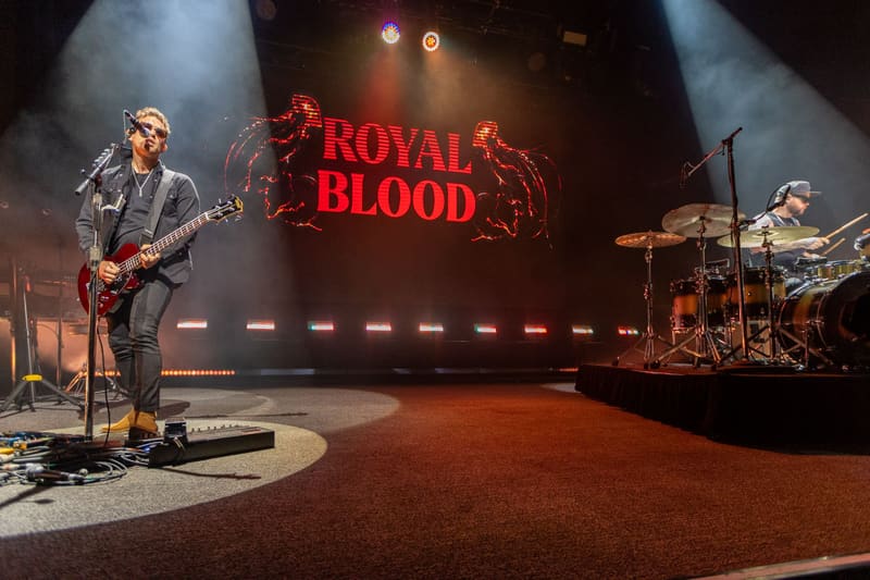 Guitarist and drummer perform on stage beneath glowing "Royal Blood" signage and atmospheric lighting.