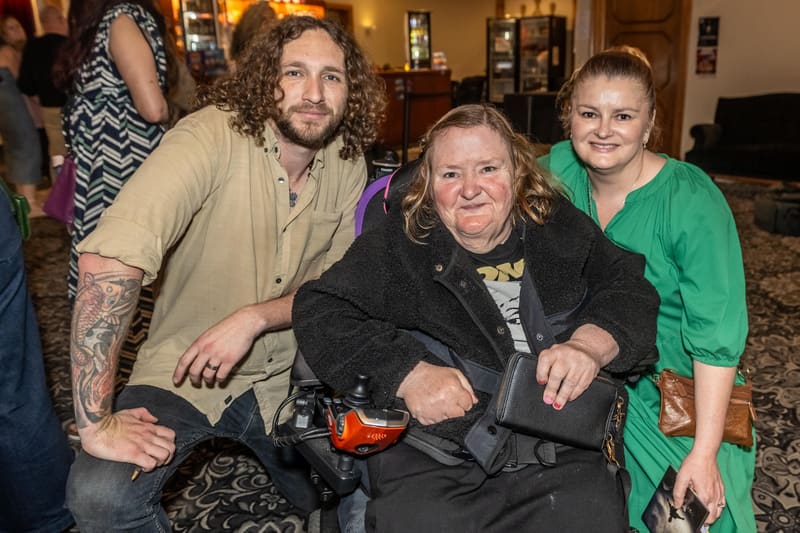 Three people pose together indoors at a gallery event, smiling at the camera.