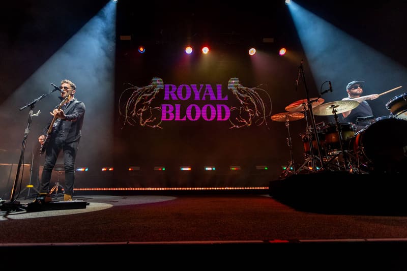 Royal Blood band performs on stage with dramatic blue spotlights and magenta logo backdrop.