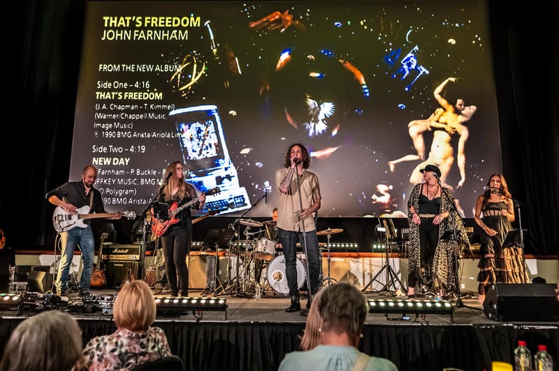Band performing on stage with projection screen displaying "That's Freedom" text and album artwork behind them.