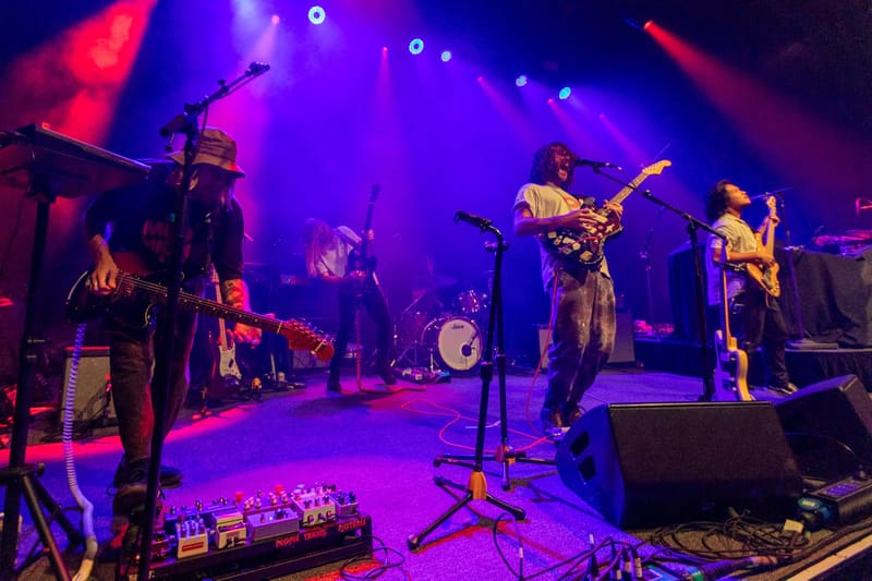 Band performs on stage bathed in vibrant purple and pink lighting during a live concert.