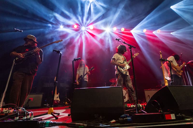 Band members perform on stage bathed in pink and blue psychedelic lighting during a Psychedelic Porn Crumpets concert.