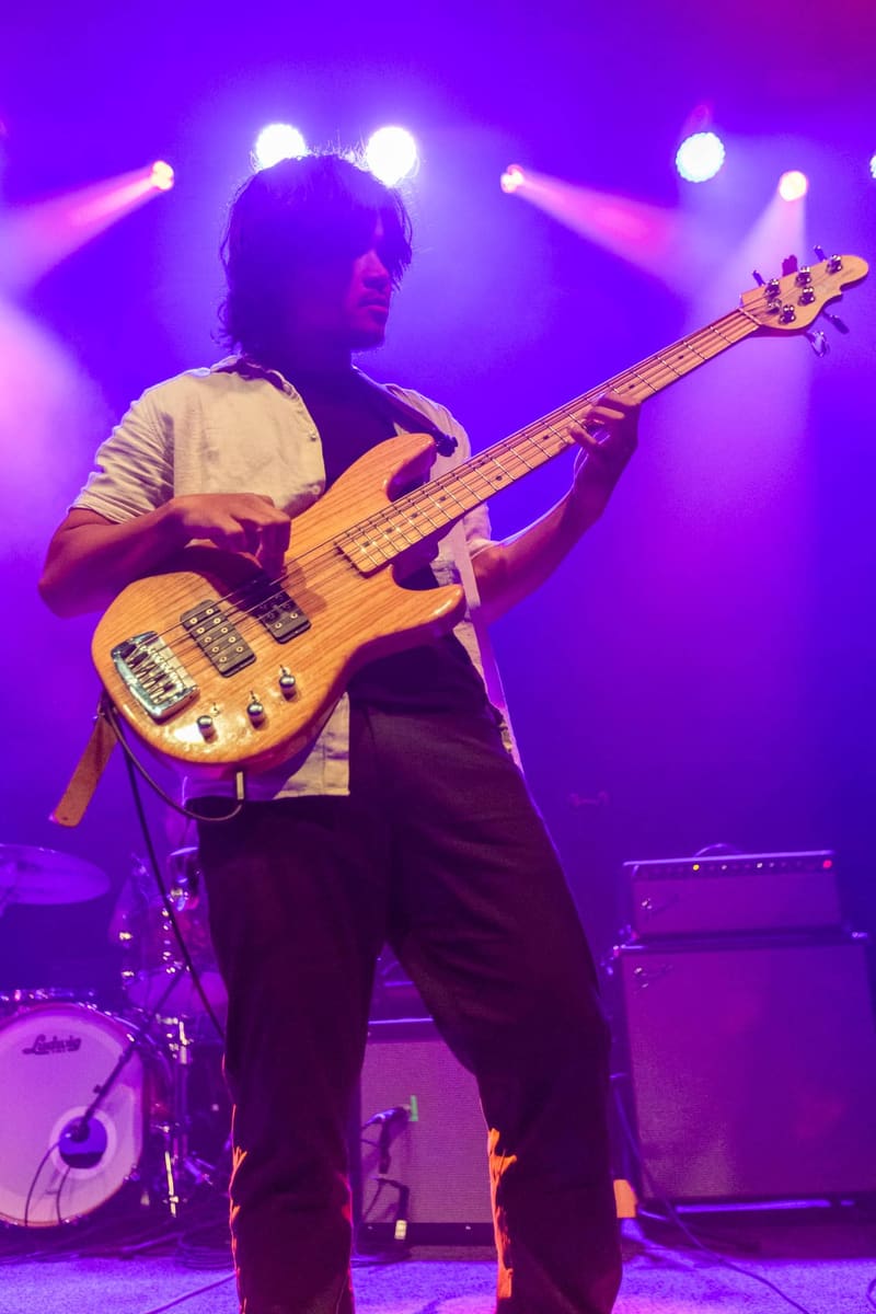 Bassist performs on stage under purple spotlights during a Psychedelic Porn Crumpets concert.