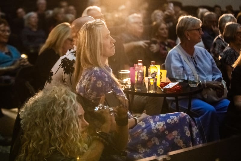 Gallery visitors seated at tables during an intimate evening event with warm overhead lighting.