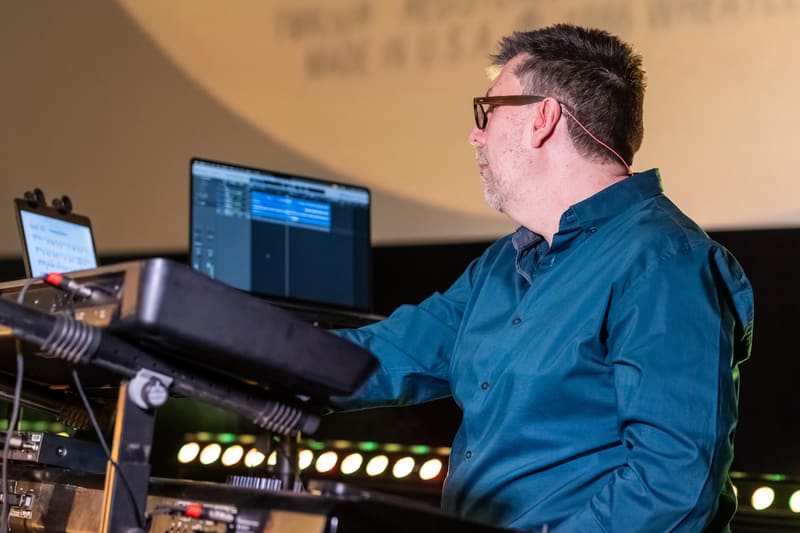 Man in blue shirt operating sound equipment and monitors at a gallery event.