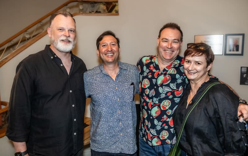 Four people stand together smiling at Gallery Three, with artwork visible on the walls behind them.